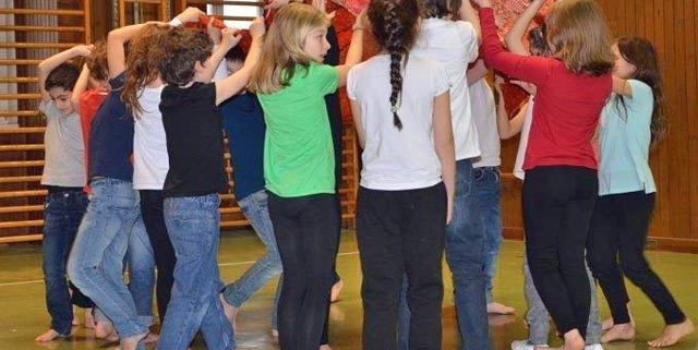 Eine Gruppe von Kindern führt in einem Turnsaal einen Tanz mit Tüchern auf
