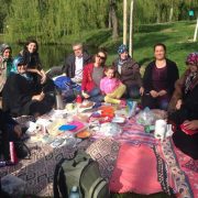 8 türkische Teilnehmerinnen und eine Tochter sitzen mit der Psychologin und dem Ernährungsmediziner auf einer Picknickdecke im Park und genießen eine gesunde Mahlzeit