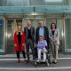 Drei Frauen, davon eine sitzend im Rollstuhl, eine mit Beinprotese, und zwei Männer befinden sich vor dem Zugang mit Lift zum Donauspital