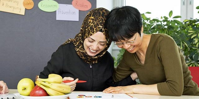 Zwei Frauen blicken in einem Schulungsraum gemeinsam in Arbeitsunterlagen