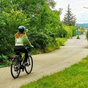 Eine junge Frau fährt auf einem Fahrrad einen Radweg entlang, rundherum ist es grün