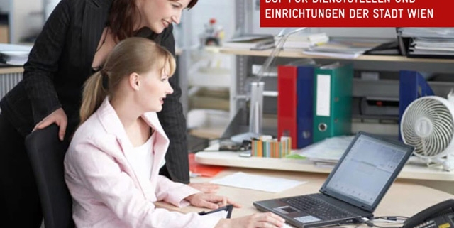 2 Frauen blicken auf einen Bildschirm, eine sitzt, die andere steht hinter der ersten und stützt sich auf den Schreibtisch. In einem Textfeld über dem Laptop steht: „BGF für Dienststellen und Einrichtungen der Stadt Wien“