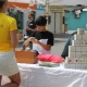 Eine junge Frau von hinten steht vor einem Tisch mit verschiedenen Ausstellungstücken, unter anderem eine Ernährungspyramide aus Kartonwürfeln. Davor steht ein Junge, der sich mit den Materialien beschäftigt.